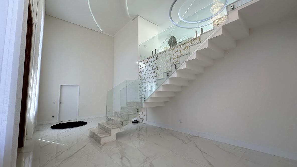 Escada de mármore com guarda-corpo de vidro e painel decorativo no hall em pé-direito duplo